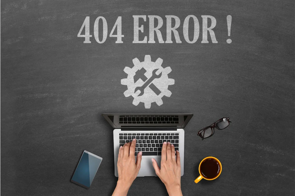 Hands typing on a laptop with "404 ERROR!" and a gear icon above, next to a phone, glasses, and coffee.